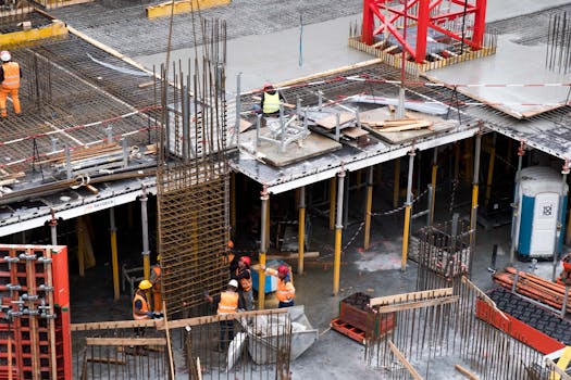 Home Workers in high visibility gear at a busy construction site with scaffolding and steel frames.