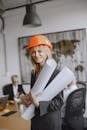 Smiling female architect in hard hat holding blueprints in modern office setting.