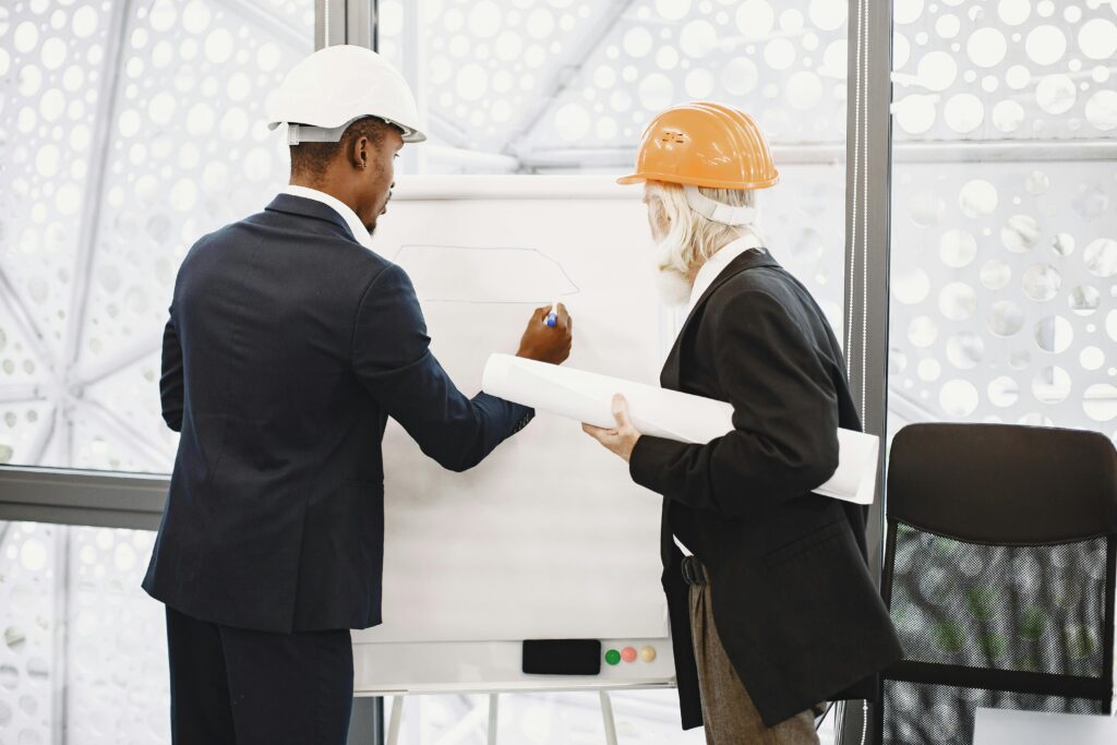 Two architects in hard hats working on a blueprint indoors, highlighting teamwork.